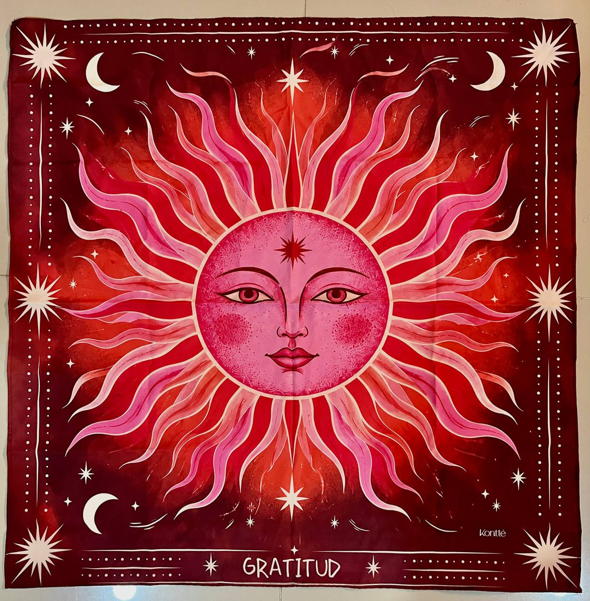 Pañoleta Gratitud en rojo y rosa con un sol de rostro ilustrado, lunas y estrellas en crema.